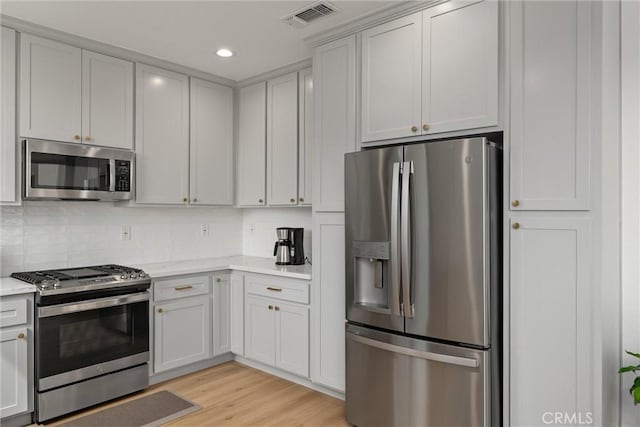 kitchen with tasteful backsplash, light stone countertops, light hardwood / wood-style flooring, and appliances with stainless steel finishes