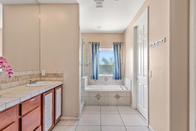 bathroom with a relaxing tiled tub, vanity, and tile patterned floors