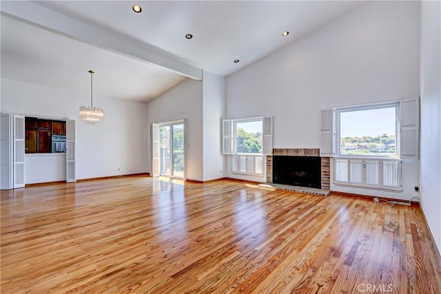 unfurnished living room featuring a brick fireplace, a notable chandelier, light wood-type flooring, high vaulted ceiling, and beam ceiling