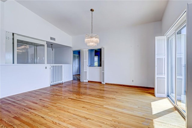 empty room with high vaulted ceiling, a chandelier, and light hardwood / wood-style flooring