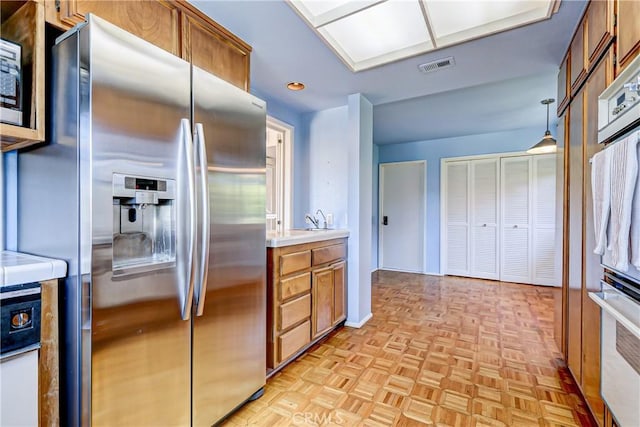 kitchen with decorative light fixtures, light parquet floors, stainless steel fridge, and sink