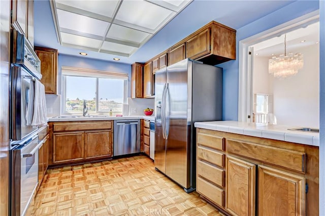 kitchen featuring stainless steel appliances, sink, tile countertops, a chandelier, and light parquet floors