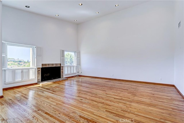 unfurnished living room featuring a brick fireplace, a towering ceiling, and light hardwood / wood-style floors