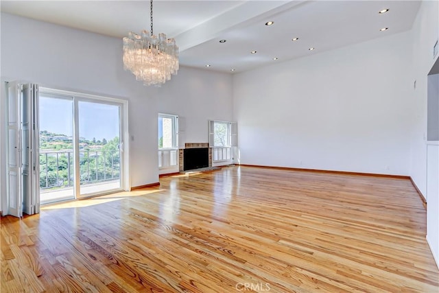 unfurnished living room with light wood-type flooring, a notable chandelier, a wealth of natural light, and a high ceiling