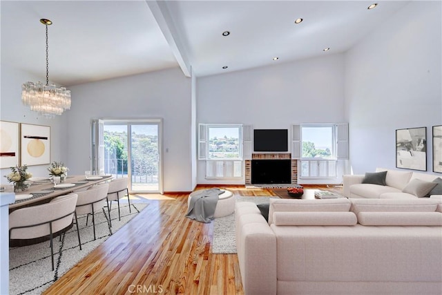 living room featuring light wood-type flooring, a brick fireplace, an inviting chandelier, and a towering ceiling