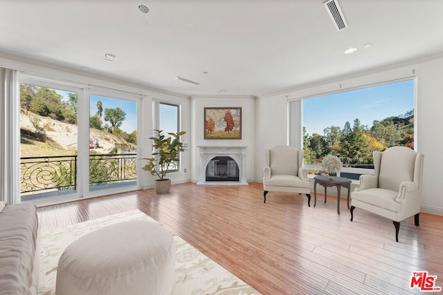 living room featuring ornamental molding, a wealth of natural light, a fireplace, and light wood-type flooring