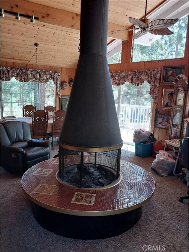 living room featuring wood ceiling, wood walls, a wood stove, ceiling fan, and carpet