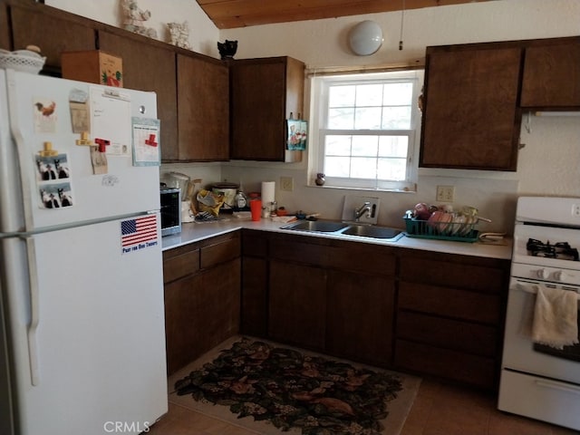 kitchen featuring light tile patterned flooring, white appliances, lofted ceiling, dark brown cabinetry, and sink