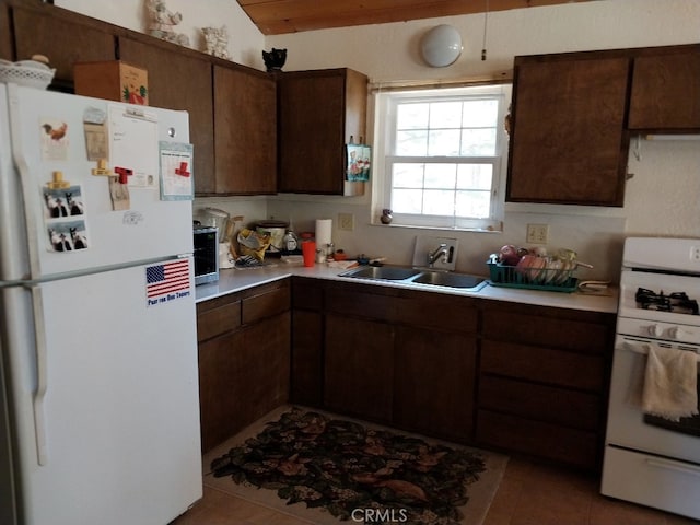 kitchen featuring vaulted ceiling, white appliances, light tile patterned floors, dark brown cabinetry, and sink