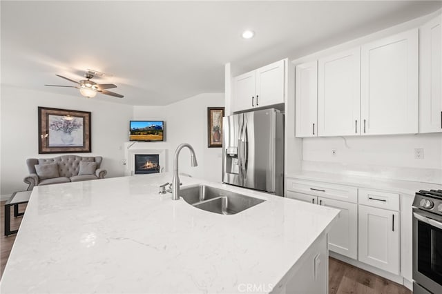 kitchen with appliances with stainless steel finishes, open floor plan, a sink, and light stone countertops