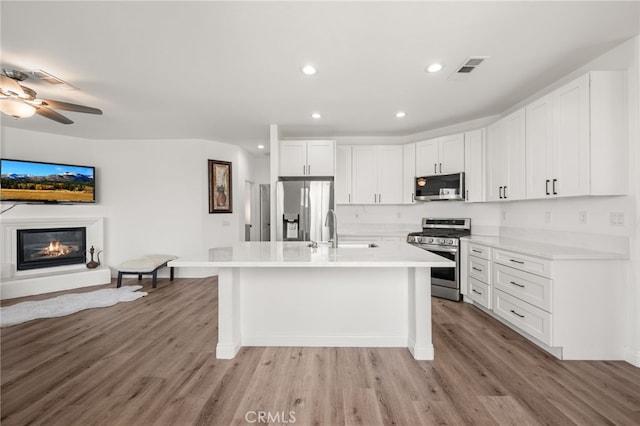 kitchen featuring stainless steel appliances, white cabinets, light countertops, and a center island with sink