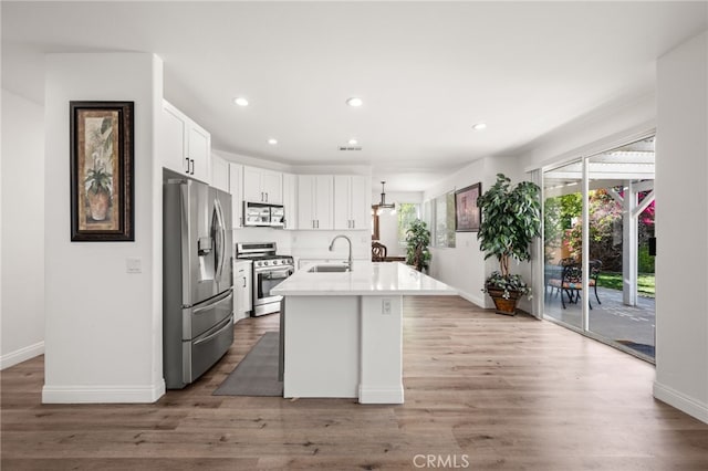 kitchen with a sink, white cabinetry, light countertops, appliances with stainless steel finishes, and a center island with sink