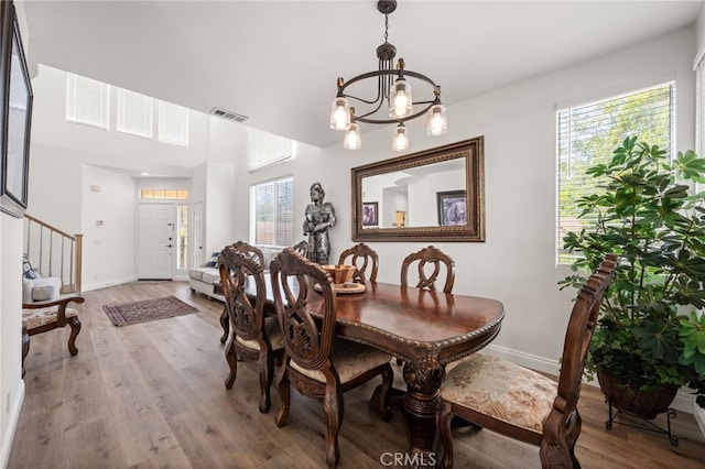 dining space featuring a chandelier, wood finished floors, visible vents, baseboards, and stairs