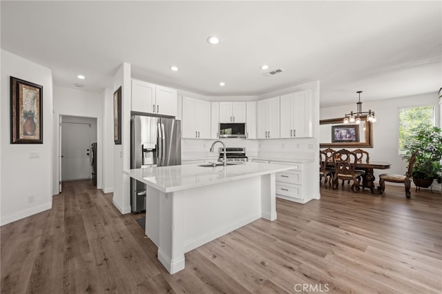 kitchen with decorative light fixtures, stainless steel appliances, visible vents, a kitchen island with sink, and white cabinets