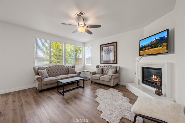 living room featuring visible vents, a ceiling fan, a glass covered fireplace, wood finished floors, and baseboards