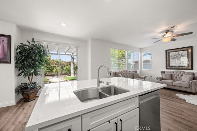 kitchen with stainless steel dishwasher, open floor plan, a kitchen island with sink, white cabinets, and a sink