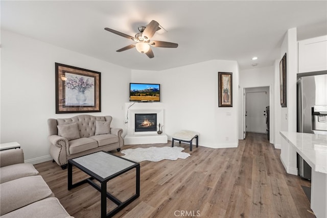 living area with light wood-style flooring, baseboards, ceiling fan, and a glass covered fireplace