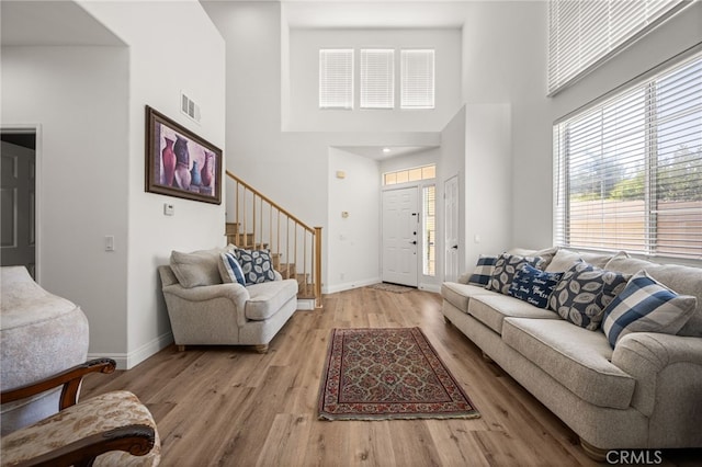 living room featuring light wood finished floors, visible vents, stairway, a high ceiling, and baseboards