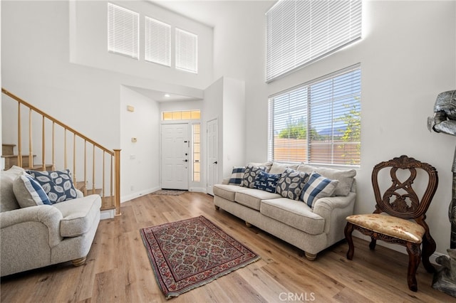 living area with a high ceiling, stairway, light wood-type flooring, and baseboards