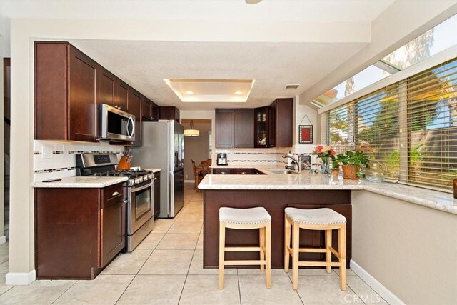 kitchen with sink, kitchen peninsula, appliances with stainless steel finishes, a tray ceiling, and a breakfast bar area