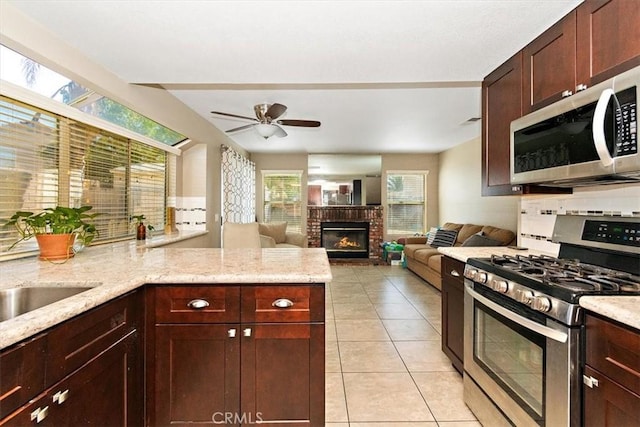 kitchen with light tile patterned floors, stainless steel appliances, a brick fireplace, ceiling fan, and a peninsula