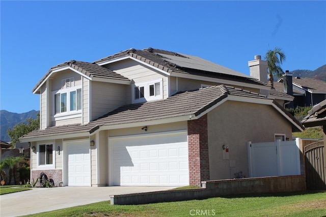 front of property with a garage, solar panels, a mountain view, and a front lawn