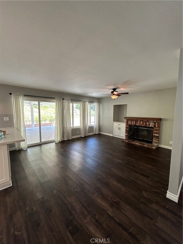 unfurnished living room featuring a brick fireplace, ceiling fan, and dark hardwood / wood-style floors