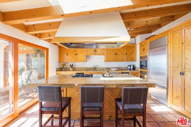 kitchen with vaulted ceiling with beams, stainless steel appliances, island range hood, and a breakfast bar area