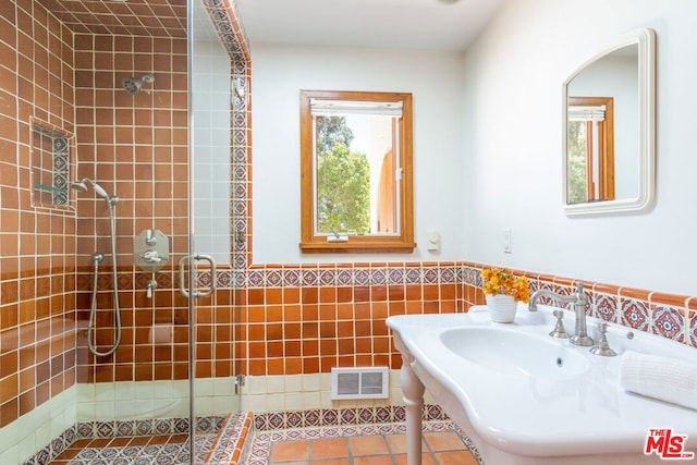 bathroom with a shower with door, sink, tile walls, and a wealth of natural light