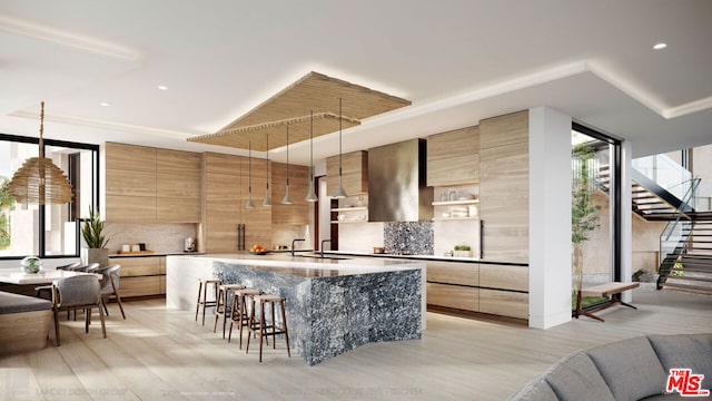 kitchen with decorative backsplash, an island with sink, a kitchen breakfast bar, light wood-type flooring, and pendant lighting