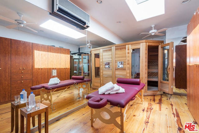 sitting room with a skylight, ceiling fan, a wall mounted AC, and light hardwood / wood-style flooring