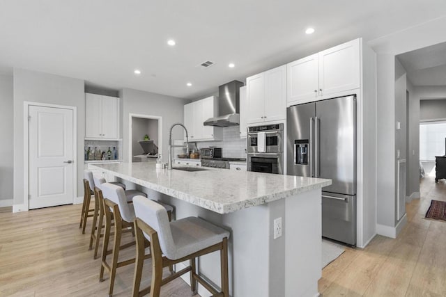 kitchen with a center island with sink, a breakfast bar, sink, stainless steel appliances, and wall chimney exhaust hood