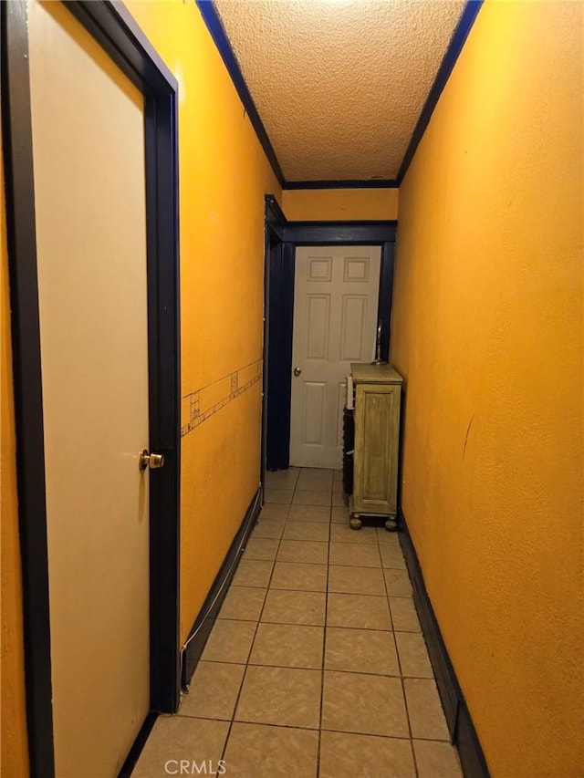 hallway featuring a textured ceiling, crown molding, and light tile patterned flooring