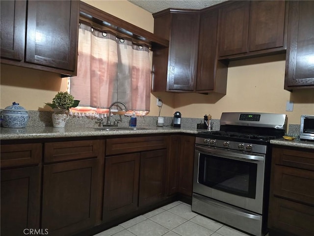 kitchen featuring sink, light tile patterned floors, a textured ceiling, dark brown cabinetry, and stainless steel range with gas stovetop