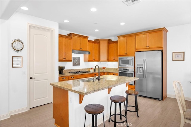 kitchen featuring stainless steel appliances, light hardwood / wood-style flooring, light stone counters, and a center island with sink