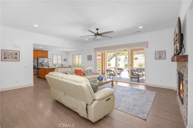 living room featuring light wood-type flooring, ceiling fan, and a fireplace