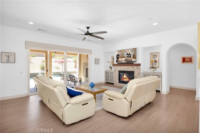 living room with ceiling fan, light hardwood / wood-style flooring, and a stone fireplace