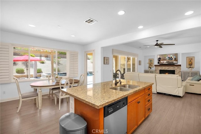 kitchen with dishwasher, ceiling fan, sink, light stone countertops, and an island with sink