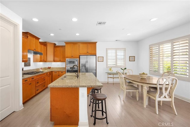 kitchen featuring appliances with stainless steel finishes, sink, light stone countertops, a kitchen bar, and a kitchen island with sink