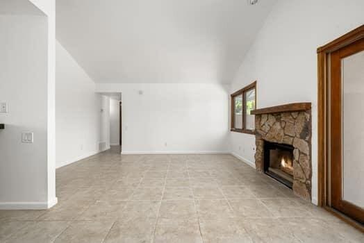 unfurnished living room with a fireplace, vaulted ceiling, and light tile patterned floors