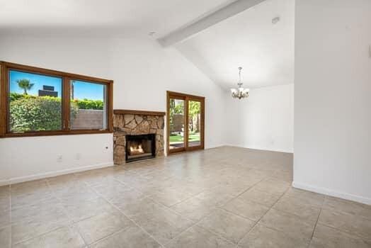 unfurnished living room featuring a healthy amount of sunlight, a stone fireplace, high vaulted ceiling, and a notable chandelier