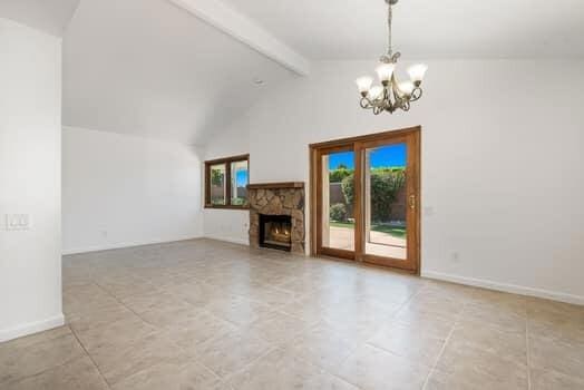 unfurnished living room featuring a fireplace, lofted ceiling with beams, and an inviting chandelier