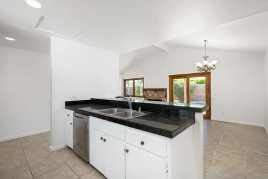 kitchen featuring dishwasher, sink, white cabinets, vaulted ceiling, and kitchen peninsula