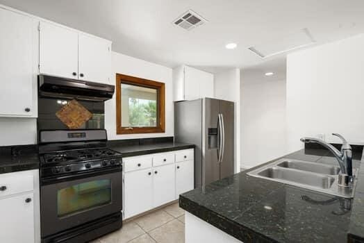 kitchen featuring light tile patterned flooring, stainless steel fridge, sink, white cabinetry, and gas stove