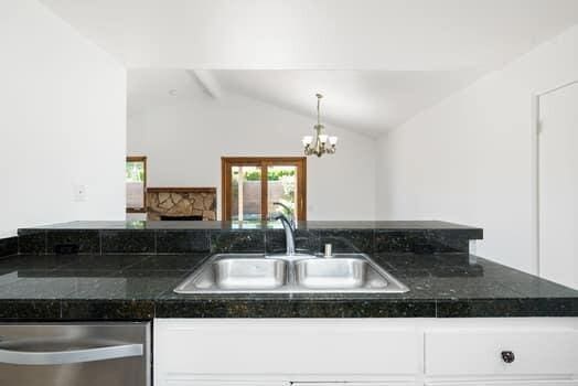 kitchen with white cabinetry, dishwasher, lofted ceiling, sink, and a chandelier