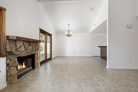 unfurnished living room with a notable chandelier, a stone fireplace, light tile patterned floors, and high vaulted ceiling