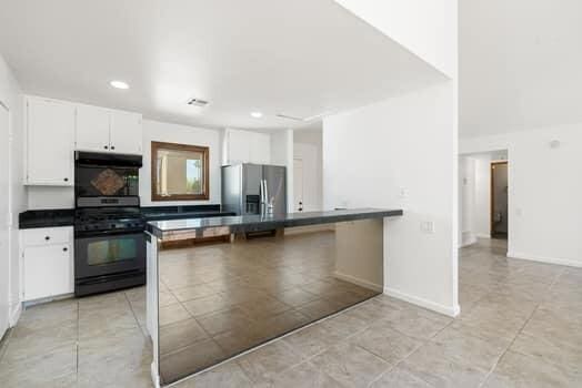 kitchen featuring white cabinets, kitchen peninsula, black gas range oven, and stainless steel fridge with ice dispenser