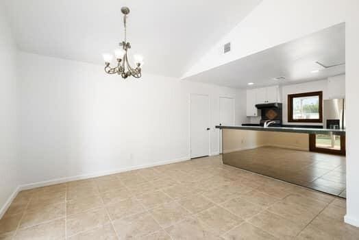 kitchen with white cabinets, lofted ceiling, hanging light fixtures, stainless steel fridge, and an inviting chandelier