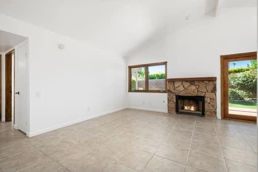 unfurnished living room featuring a stone fireplace, light tile patterned floors, and high vaulted ceiling