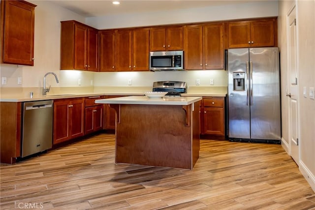 kitchen with a kitchen island, appliances with stainless steel finishes, a breakfast bar, sink, and light wood-type flooring